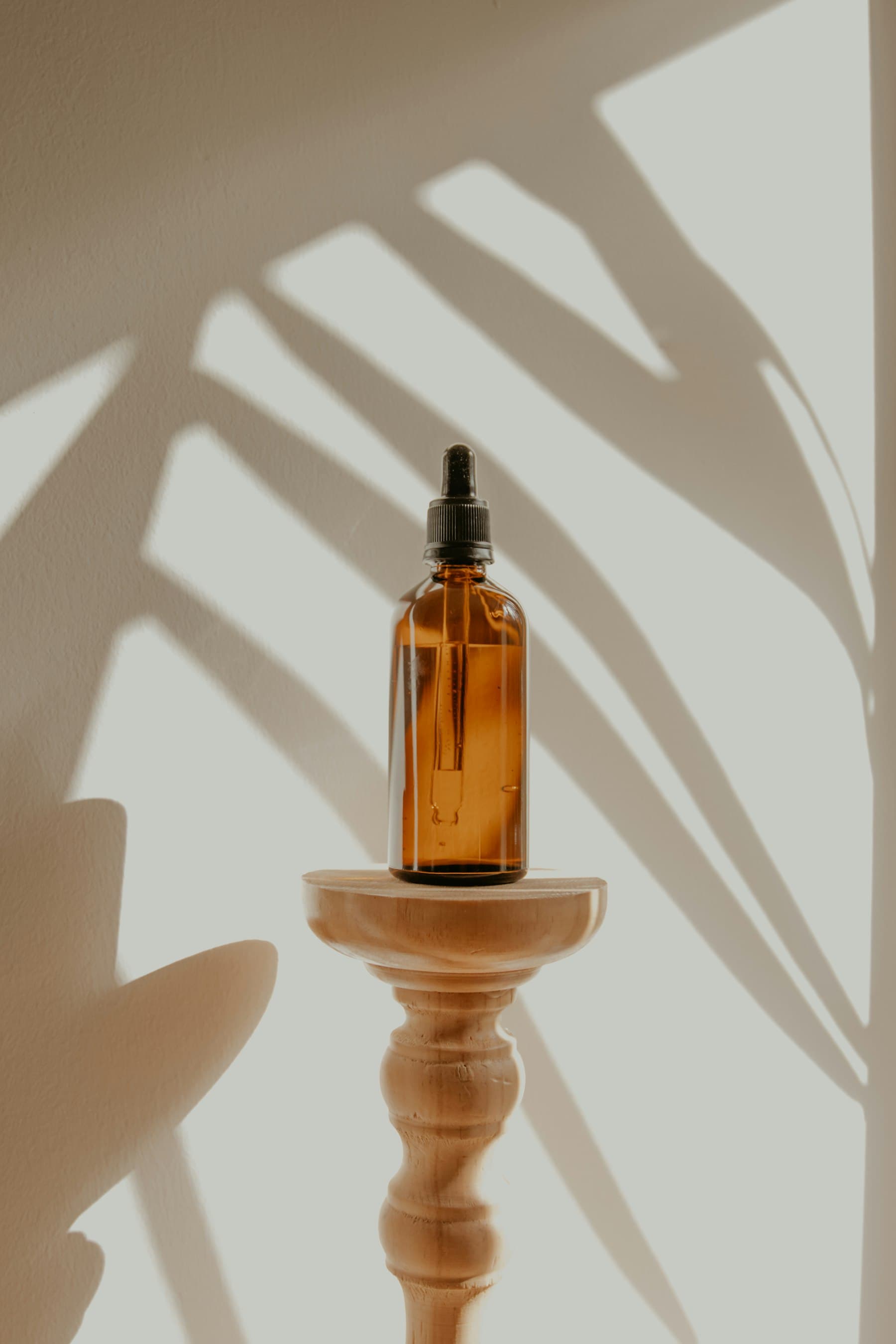 Amber glass dropper bottle of kernel oil on a wooden stand, framed by leaf shadows