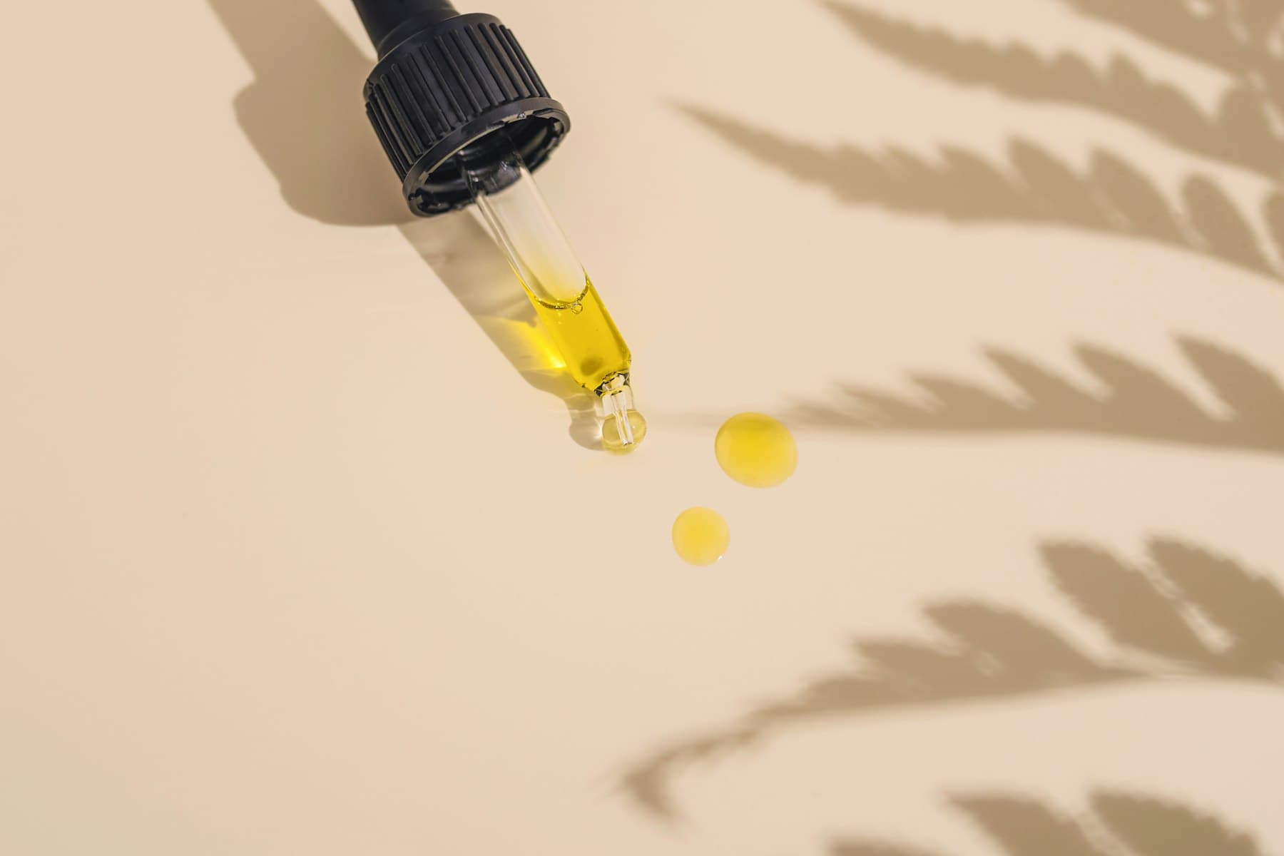 Golden oil falling from a glass dropper beside leaf shadows